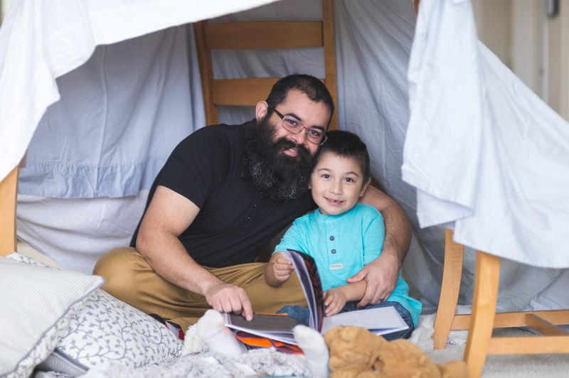 man and little boy reading a book in a homemade tent
