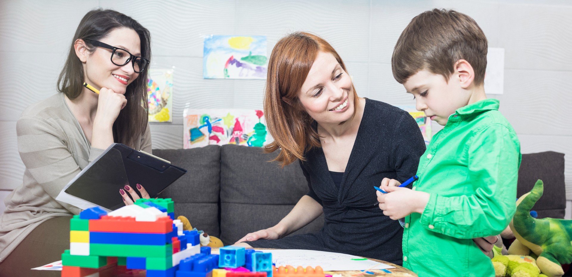 two adults watching a little boy play with building blocks