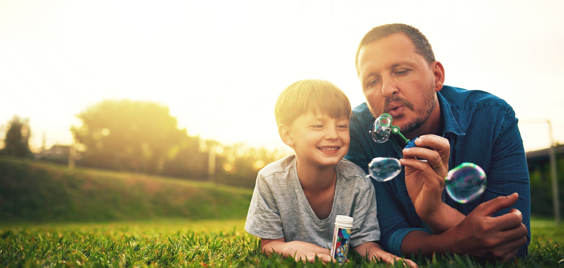 man and child laying on grass blowing bubbles