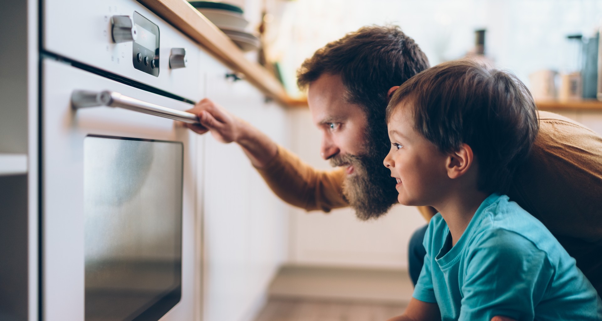 man and child looking at food cooking in an oven
