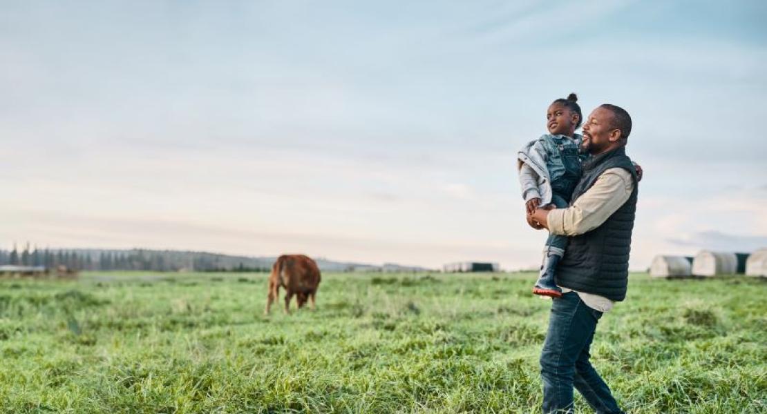 man carrying a little girl walking through a field